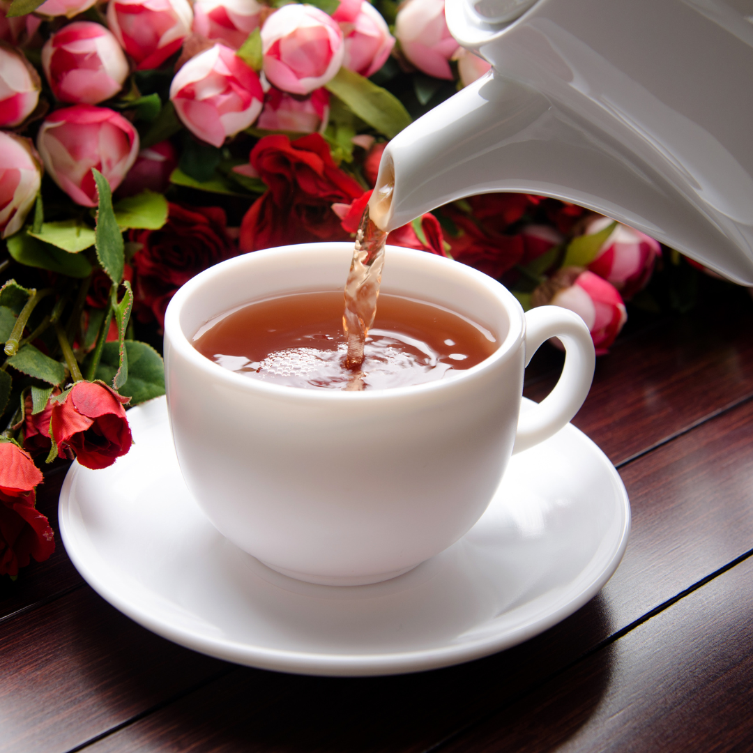 White teapot pouring tea into a white cup with a floral background