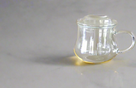 A clear glass mug with a handle, photographed against a beige background.